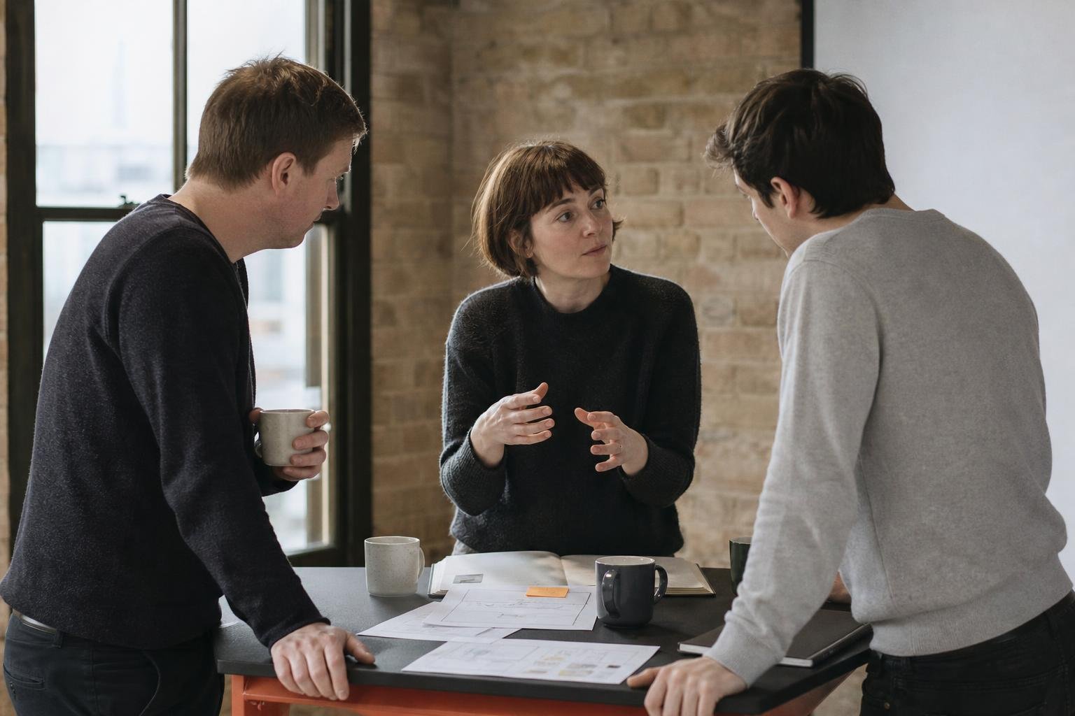 Three colleagues standing around a table discussing which SaaS PPC agency to hire
